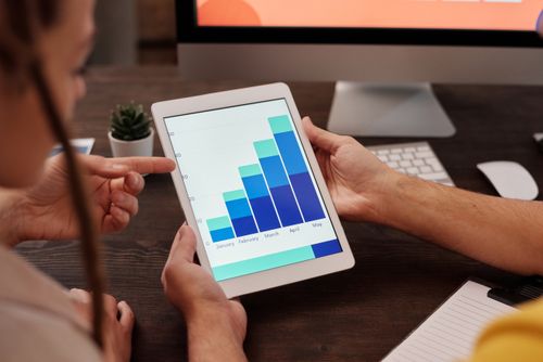 Two office workers analyzing complex graphs on a tablet screen for collaborative data analysis. Photo: Pexels.