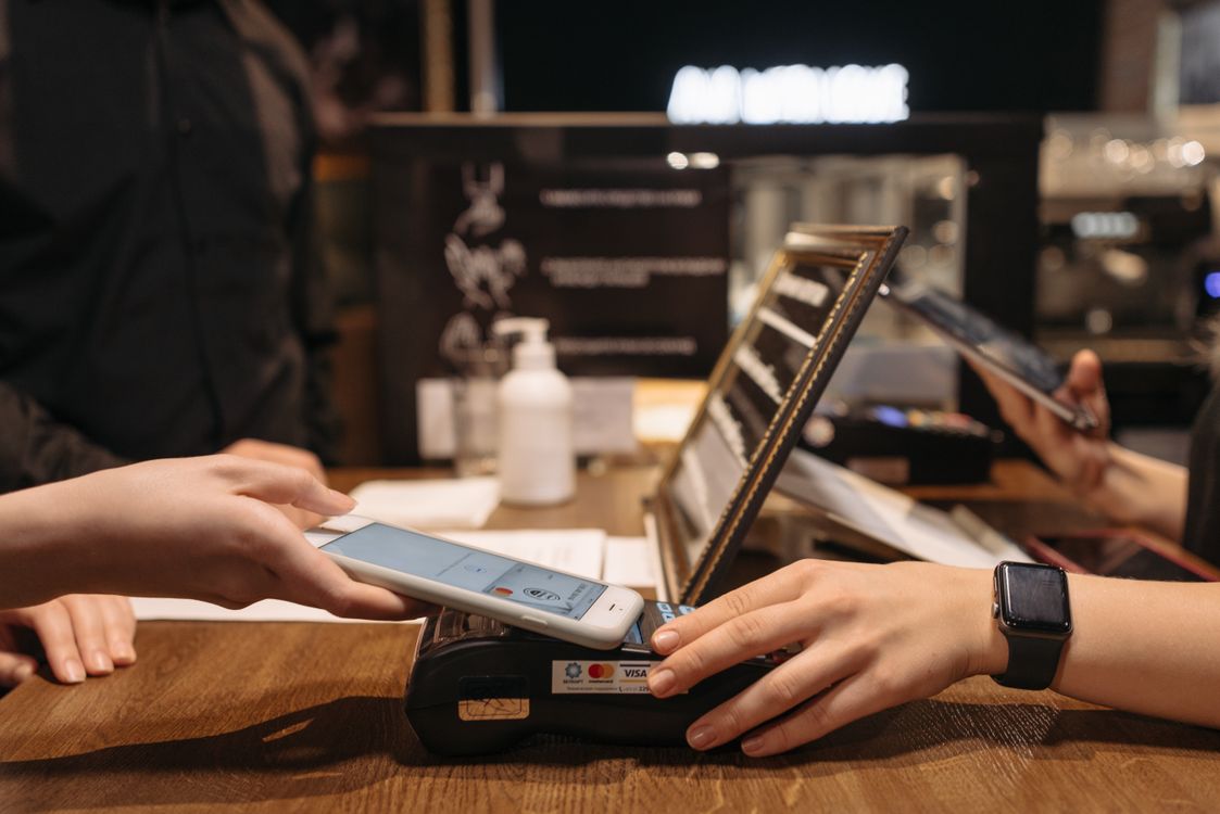 Hands utilizing a smartphone for a contactless payment mid-transaction inside a physical shop. Photo: Pexels.