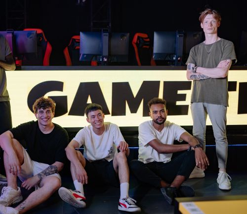 Four young players posing confidently with gaming setups in an eSports arena. Photo: Pexels.